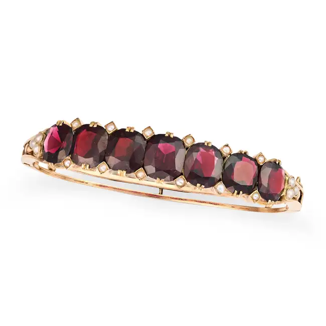 AN ANTIQUE GARNET AND PEARL BANGLE the hinged bangle set with a row of cushion cut garnets, accented