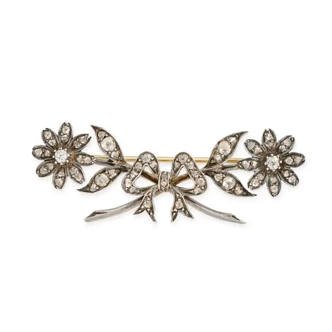 AN ANTIQUE DIAMOND BROOCH in yellow gold and silver, comprising a bow motif accented by two flowers,