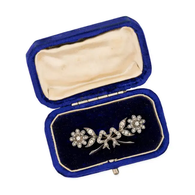 AN ANTIQUE DIAMOND BROOCH in yellow gold and silver, comprising a bow motif accented by two flowers,