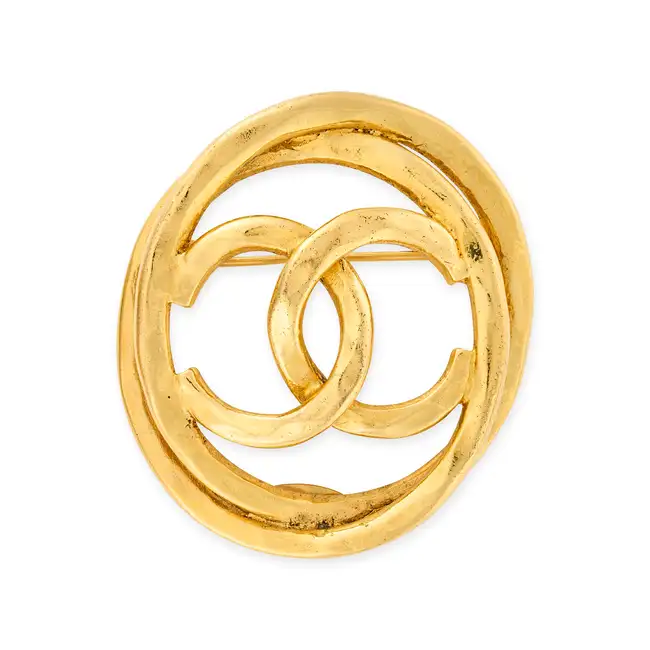 CHANEL, A CC BROOCH comprising an oval textured gold tone metal brooch with an interlocking CC