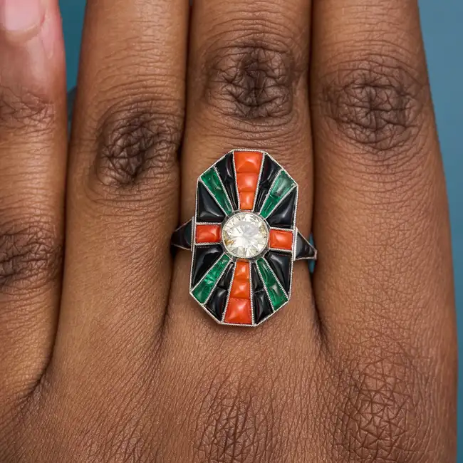 AN ART DECO DIAMOND, CORAL, ONYX AND EMERALD DRESS RING set with a round brilliant cut diamond of