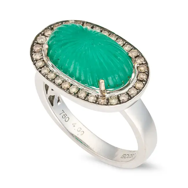 A CARVED EMERALD AND DIAMOND RING set with a carved cabochon emerald of 4.69 carats, within a border