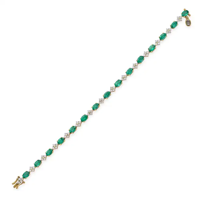 AN EMERALD AND DIAMOND BRACELET in 18ct yellow gold, comprising a row of oval cut emeralds, accented