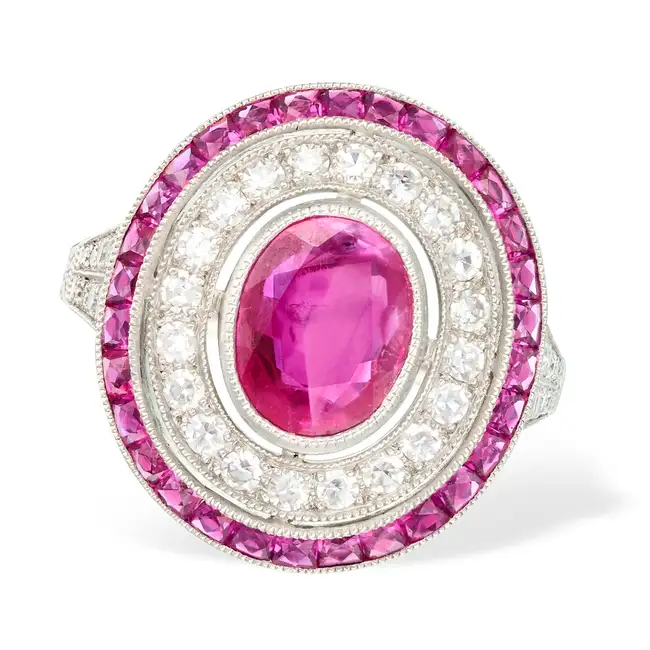 A RUBY AND DIAMOND TARGET RING set with an oval cut ruby of 1.66 carats, within a border of single