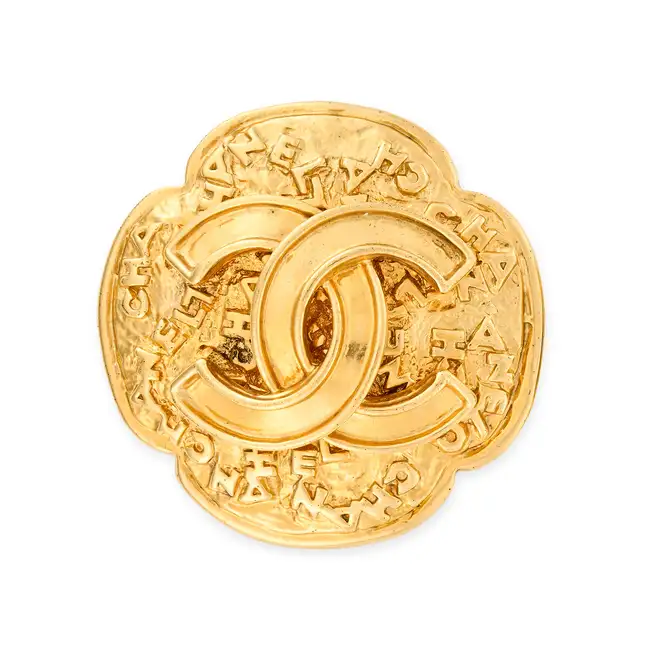 CHANEL, A CC BROOCH comprising a textured gold tone metal brooch with an interlocking CC logo in the