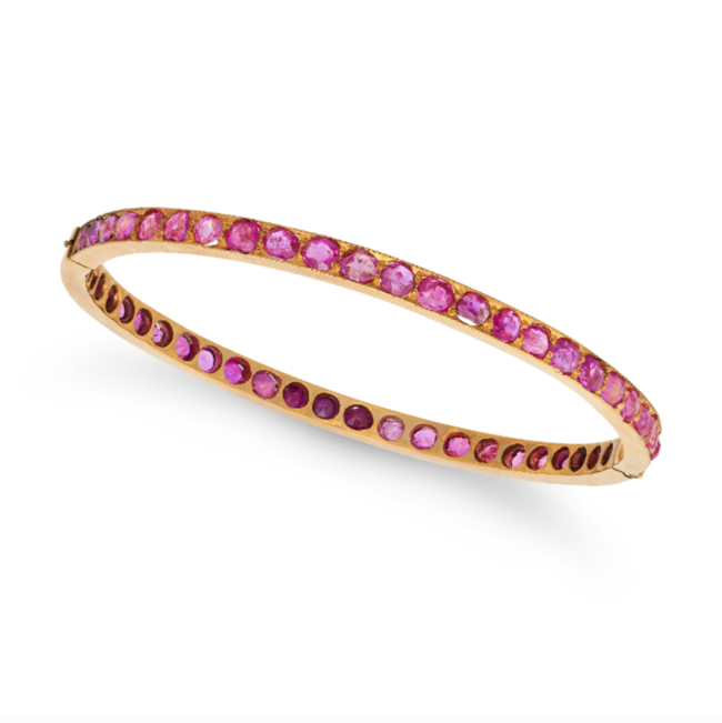A BURMA NO HEAT RUBY BANGLE in 18ct yellow gold, the hinged bangle set all around with a row of oval and round cut rubies all totalling 7.0-7.5 carats, no assay marks, inner circumference 16.0cm, 11.8g. Accompanied by a gemmological report stating th
