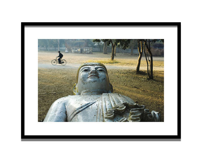 
	
		Steve McCurry,
		American b.1950-
		 
		A Man Rides Past a Buddha Statue in a Park,...