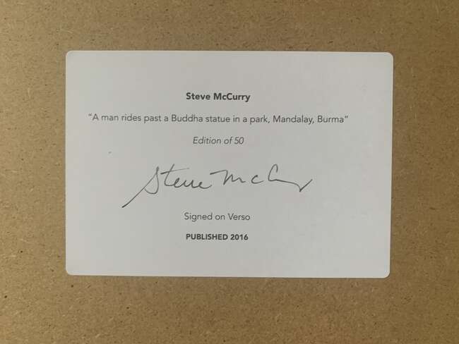 
	
		Steve McCurry,
		American b.1950-
		 
		A Man Rides Past a Buddha Statue in a Park,...