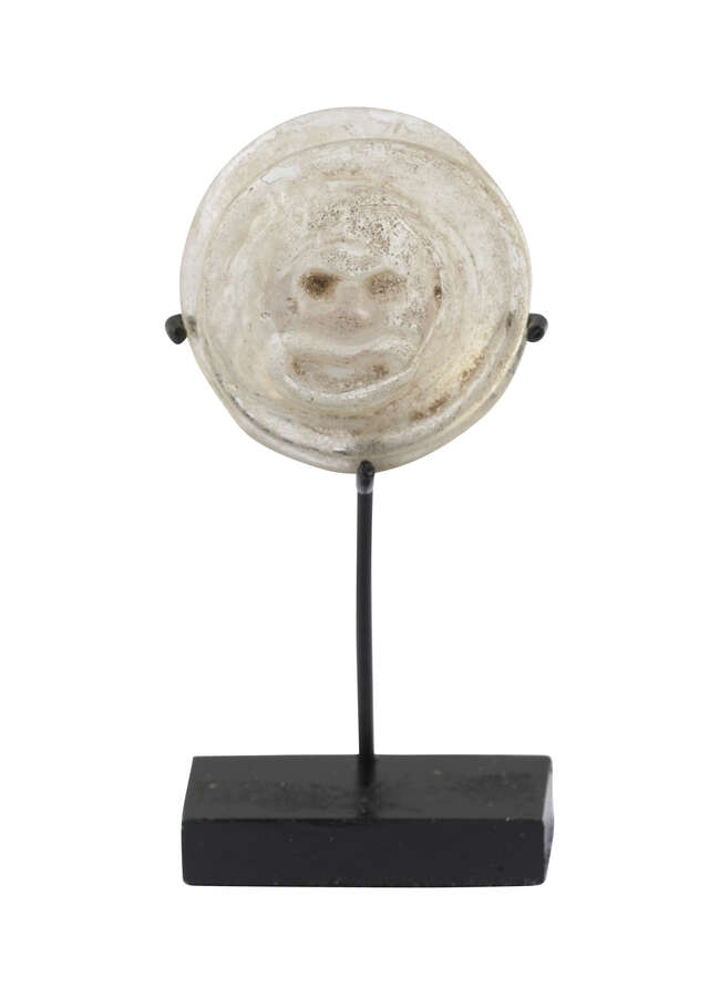 
	
		A Roman glass theatre token depicting a theatre mask, 1st-3rd century AD, on stand, 3cm....