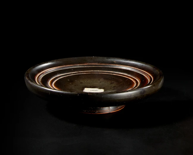 A Greek black-glazed pottery plateSouth Italy, Circa 4th century BC
A footed plate with a deep,...
