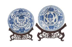 A pair of Chinese porcelain dishes, Kangxi, painted in underglaze blue with flowering lotus scrolls, 13cm diameter, on two carved hardwood plate stands
		 
