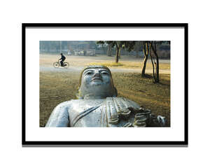 
	
		Steve McCurry,
		American b.1950-
		 
		A Man Rides Past a Buddha Statue in a Park,...