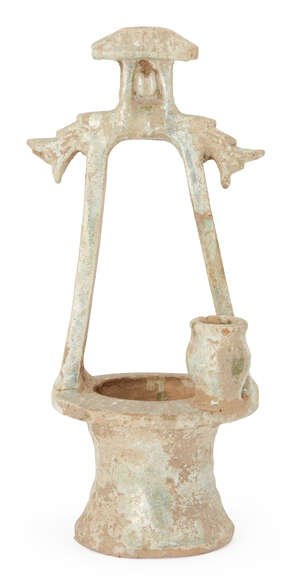 A Chinese pottery model of a well, Han dynasty, with dragon-head terminals, a jar surmounted on edge of well, and traces of green glaze with iridescence, 36.5c