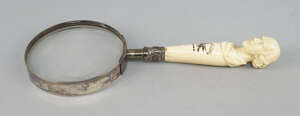 
	
		A Victorian metal magnifying glass, the carved figural ivory handle decorated with the...