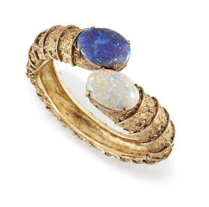 
	
		An opal two stone bangle, of hinged crossover design, the textured hoop terminating in...