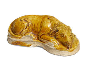 A Chinese pottery amber glazed dog, Tang dynasty, modelled in a recumbent pose with curved body, the head resting between its front paws, the long tail curled 