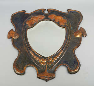 
	
		An Arts and Crafts style copper cartouche form mirror, with a shield shaped mirror,...