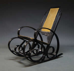 
	
		An Art Deco ebonised and caned rocking chair, the backrest with stepped top and carved...