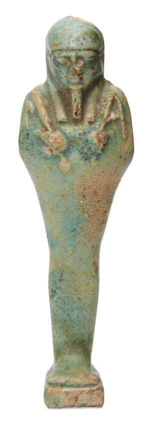 An Egyptian green glazed composition shabti, the uninscribed body depicted holding a pick and hoe relief, a seed-bag behind the left shoulder, Late Period, aft