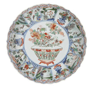 A Chinese porcelain moulded dish, Kangxi period, painted in famille verte enamels with a jardiniere of flowers surrounded by panels of landscapes, 24.5cm diame