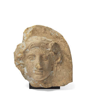 A Greek terracotta antefix with the head of Io, Taranto, circa 4th Century B.C., the nymph depicted with cow's horns, now largely lost, her wavy hair bound