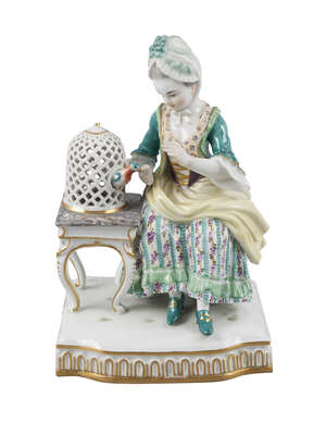 A Meissen figure of a seated lady, late 19th/early 20th century, emblematic of Touch from a Series of the Senses, wearing a green jacket, bodice, and flowered 