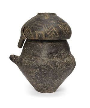 A Villanovan impasto ware biconical urn and lid, circa 9th-8th Century B.C., of burnished black fabric, the neck and shoulder incised with a dotted and hatched