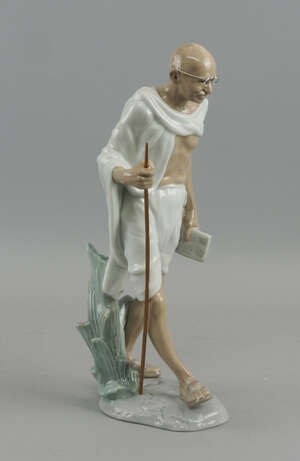 A Lladro porcelain  figure of Gandhi, late 20th century, modelled with a book and staff in his hands, draped in a cloak, marks to base, 32cm high