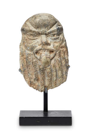 An Egyptian small stone carved head of Bes, possibly New Kingdom, 18th Dynasty, shown with furrowed brow and sticking out tongue, on metal stand, 5.6cm. high
