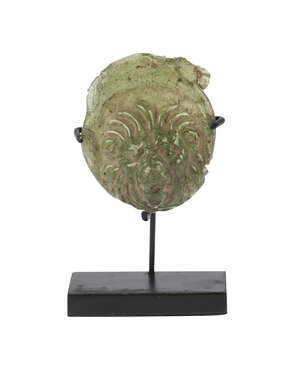 A Roman green glass token fragment in the form of a lion head, 1st-4th century AD, 4cm. high, on stand  
		 
		Provenance: Collection of George and Dora Mat