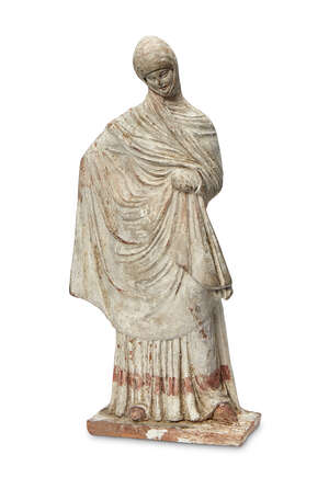 A Greek terracotta figure of a woman, Hellenistic-style, depicted standing on rectangular base, fully enveloped in a heavy wool himation over a floor-length pl