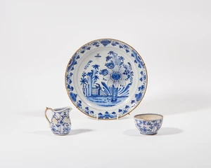 A Dutch Delft blue and white glazed earthenware plate, 18th century, the center painted with foliage and a fence within concentric double lines, the border wit