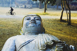 
	
		Steve McCurry, 
		American b.1950-
		 
		A Man Rides Past a Buddha Statue in a Park,...