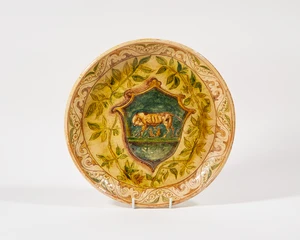An Italian glazed earthenware footed dish with 'sgraffito' decoration, probably 19th century, the well centered with a crest depicting the infant Romulus and R