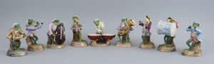 A nine piece Sitzendorf porcelain frog band, late 19th/early 20th century, each player seated on a tree stump, wearing wigs, fancy tail coats and breaches, pla