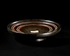 A Greek black-glazed pottery plateSouth Italy, Circa 4th century BC
A footed plate with a deep,...